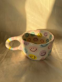 a ceramic cup with smiley faces on it sitting on a tablecloth covered surface in front of a white background