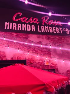 a red umbrella sitting in front of a brick wall with neon lights hanging from it