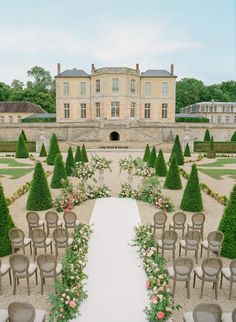 an outdoor ceremony setup with chairs and flowers in front of a large building that looks like a palace