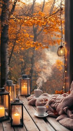 an outdoor deck with candles, blankets and coffee cup on it in front of the window