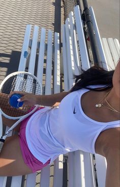 a woman holding a tennis racquet on top of a white bench next to a fence