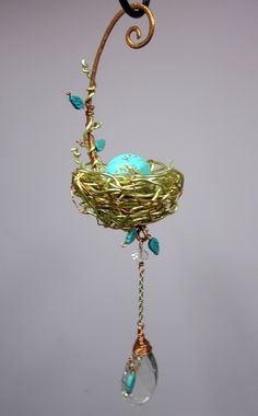 a bird's nest hanging from a metal hook with blue glass beads and gold wire