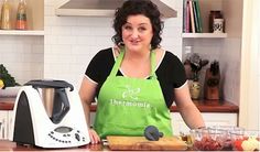 a woman standing in front of a blender on top of a kitchen counter next to a cutting board