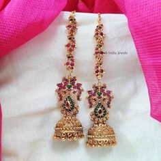 pair of gold plated earrings with red and green stones on the bottom, hanging from a pink silk scarf