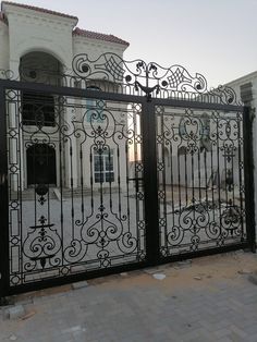 an iron gate in front of a white house with black wrought designs on the gates