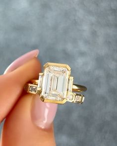 a woman's hand holding a ring with an emerald stone in the middle and two diamonds on each side