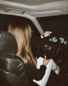 a woman sitting in the driver's seat of a car with her hand on the steering wheel