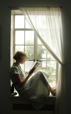 a woman sitting on a window sill reading a book