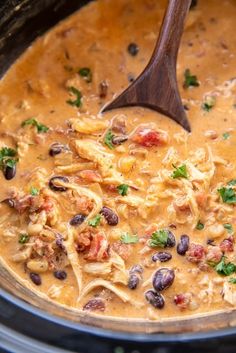 a wooden spoon in a slow cooker filled with chicken and black bean chili soup