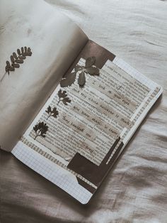 an open book sitting on top of a bed covered in sheets and paper with leaves