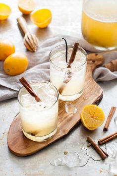 two glasses filled with drinks sitting on top of a cutting board next to oranges