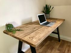 a laptop computer sitting on top of a wooden desk next to a potted plant