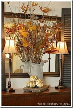 a vase filled with leaves and pumpkins sitting on top of a table next to a mirror