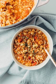 a white bowl filled with pasta and vegetables next to a pot of soup on a table