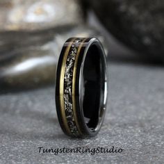 a wedding ring with black and gold inlays is shown on the ground next to a rock