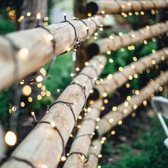 some lights are hanging on the side of a wooden fence in front of grass and trees