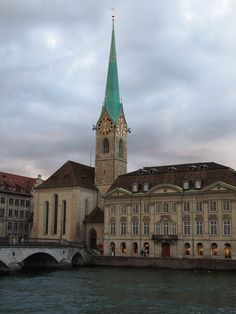 an old building with a green steeple next to the water