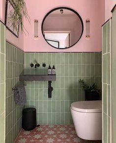 a bathroom with green and pink tiles, a mirror above the toilet and a black trash can