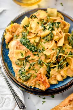 a blue plate topped with pasta and spinach covered in sauce on top of a white table