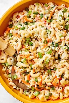 a yellow bowl filled with macaroni salad and a wooden spoon in the bowl