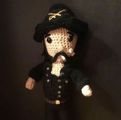 a crocheted doll is dressed in black and has a hat on it's head