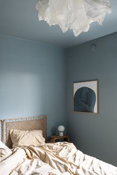 an unmade bed in a blue room with a painting on the wall above it