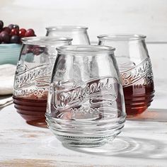 three glasses filled with liquid sitting on top of a table next to grapes and other fruit