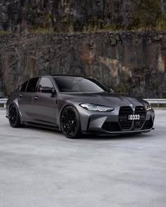 a grey bmw car parked in front of a rock wall with grass growing on it