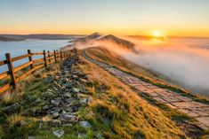 the sun is setting on top of a mountain with fog in the valley below it