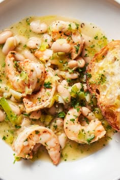 a white plate topped with shrimp and broccoli covered in gravy next to a piece of bread