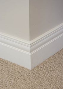 the corner of an empty room with carpet and white trim on the walls, along with a cat's paw resting on the floor