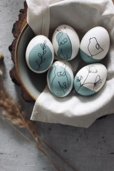 four painted eggs sitting in a bowl on top of a white cloth with the words one line art osterier