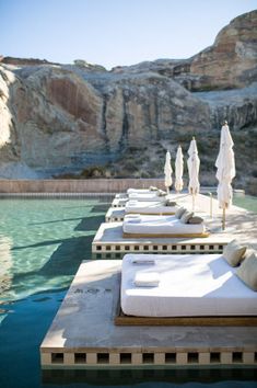 several lounge chairs and umbrellas line the edge of a pool in front of mountains