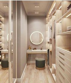 a walk - in closet with white drawers and wooden flooring, lighted by round mirrors