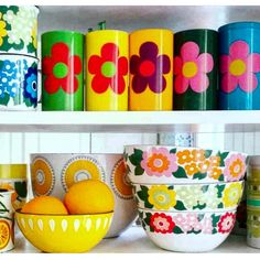 colorful bowls and containers are sitting on the shelf in front of each other with flowers painted on them