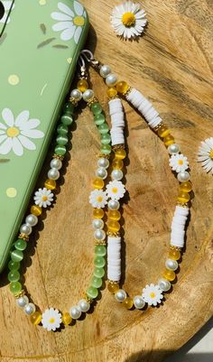 a cell phone is laying on a wooden table with beads and flowers in it's necklace