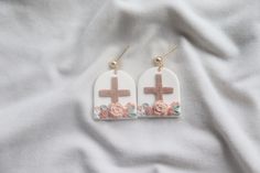 two cross shaped earrings with pink flowers on white fabric background and gold earwires