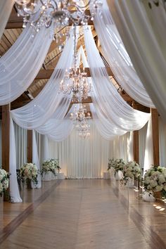 an indoor wedding venue with white drapes and chandelier draped over the aisle