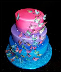 three tiered cake decorated with butterflies on blue and pink plates in front of black background