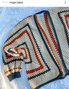 an orange and white crocheted sweater laying on top of a bed