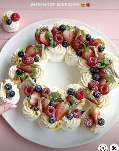 a cake decorated with strawberries and blueberries on a plate next to cupcakes