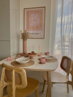 a dining room table with plates, cups and bowls on it in front of a window