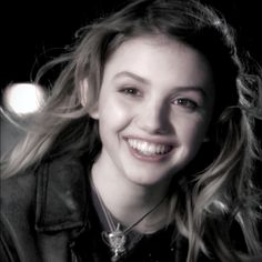 a woman with long hair smiling and wearing a leather jacket on her shoulders, she is looking at the camera