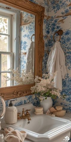 a bathroom sink sitting under a large mirror next to a white vase filled with flowers