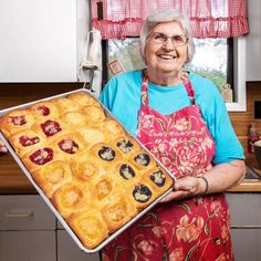 an older woman holding a pan full of baked goods