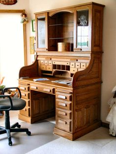 an old fashioned wooden desk in the corner of a room with a chair and window