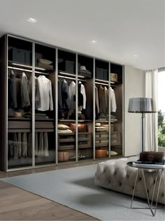 a large walk in closet with clothes on hangers and an ottoman next to it