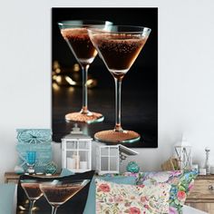 two martini glasses sitting next to each other on top of a table in front of a painting