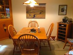 a dining room table with four chairs and a painting hanging on the wall behind it