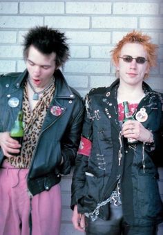 two young men standing next to each other wearing punk clothing and holding bottles in their hands